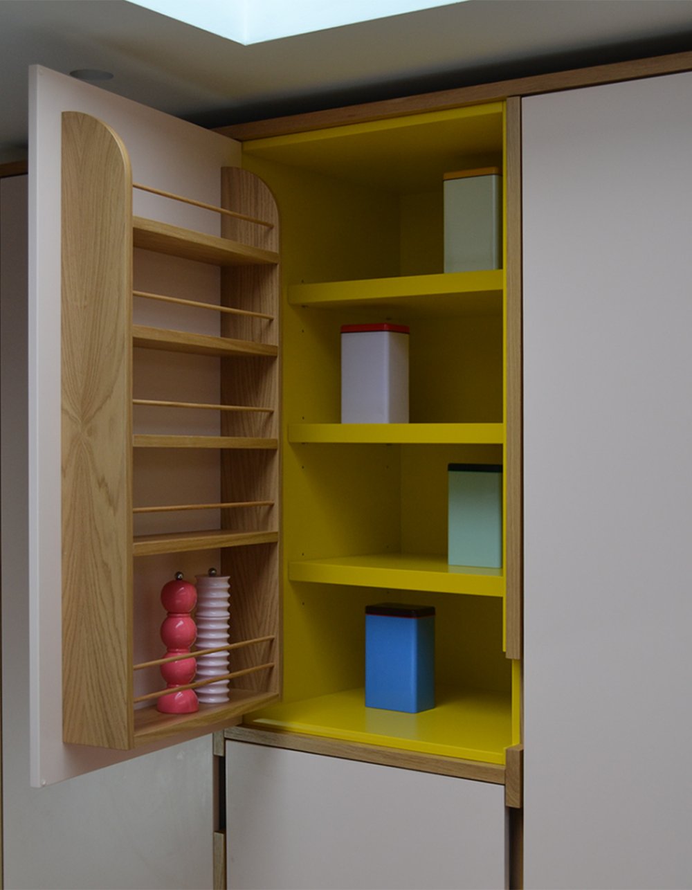 Larder cupboard open to reveal a bright yellow painted interior, with oak spice racks fitted to the inside of the door