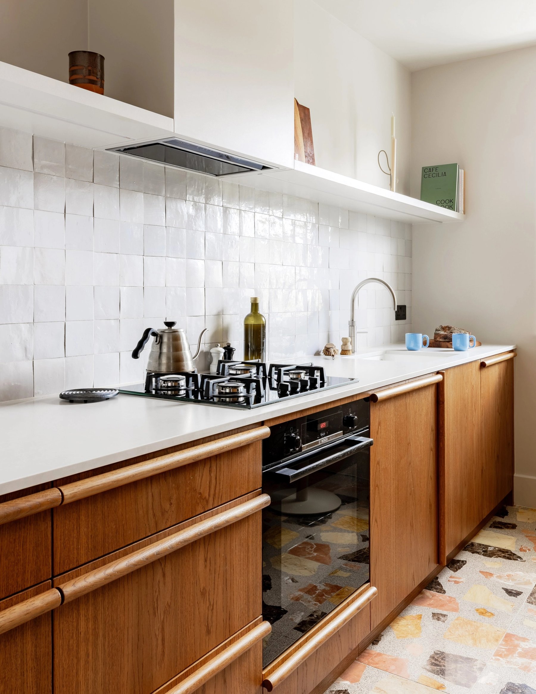 Cooking run with a gas hob and black oven set into wooden drawers, under white tiles and a slim extractor.
