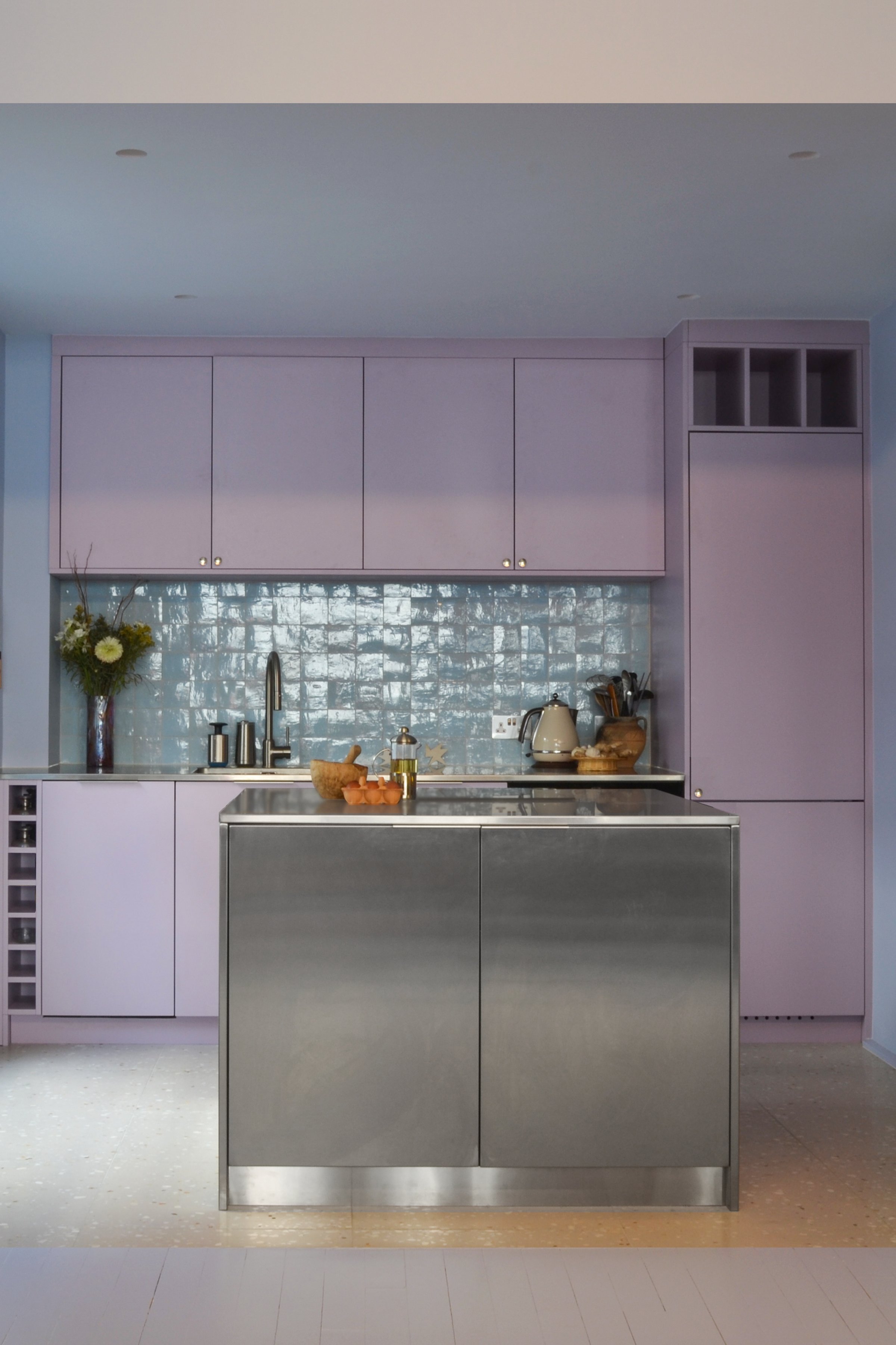 Lilac kitchen with a glazed blue-green tile splashback, a stainless steel island and a wine rack built into the end of the run