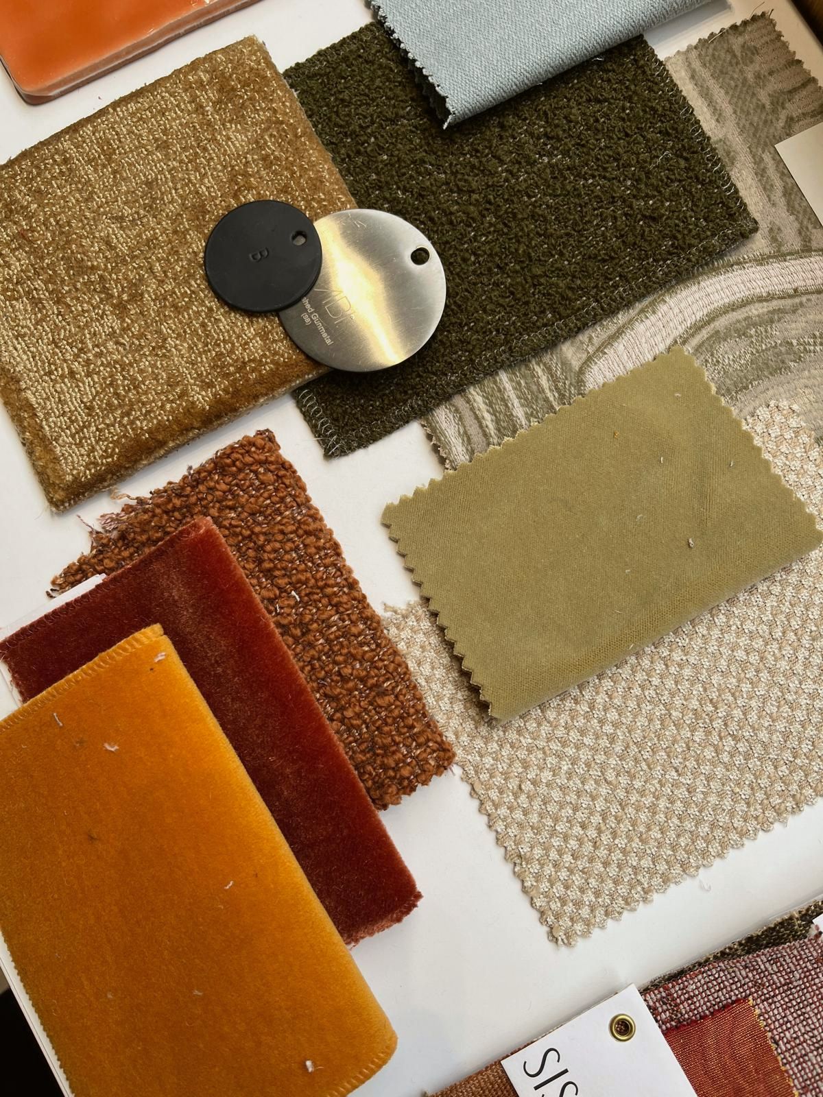 Fabric and finish samples laid out together: ochre and rust velvets, olive bouclé, textured wovens and two metal handle discs
