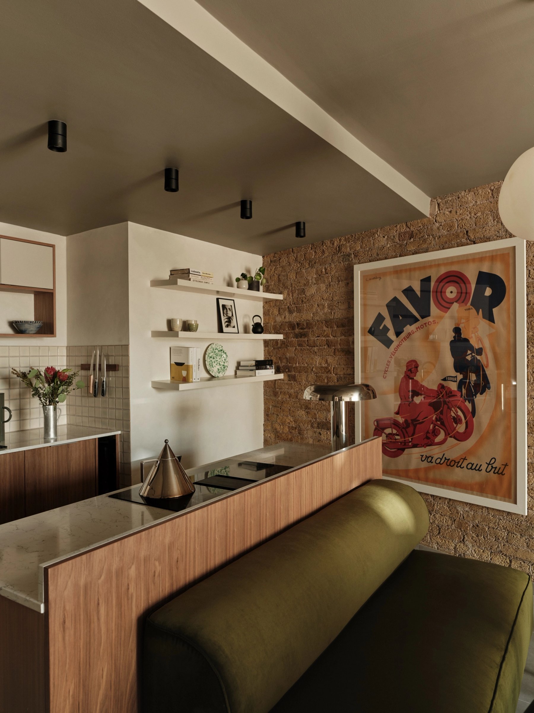 The kitchen counter from the dining side, its oak-faced back forming an olive banquette, with a stone worktop, floating shelves and square tiling.