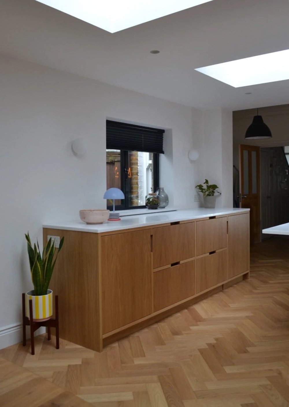 Run of oak cabinets with a white worktop below a window, standing on herringbone parquet beneath skylights