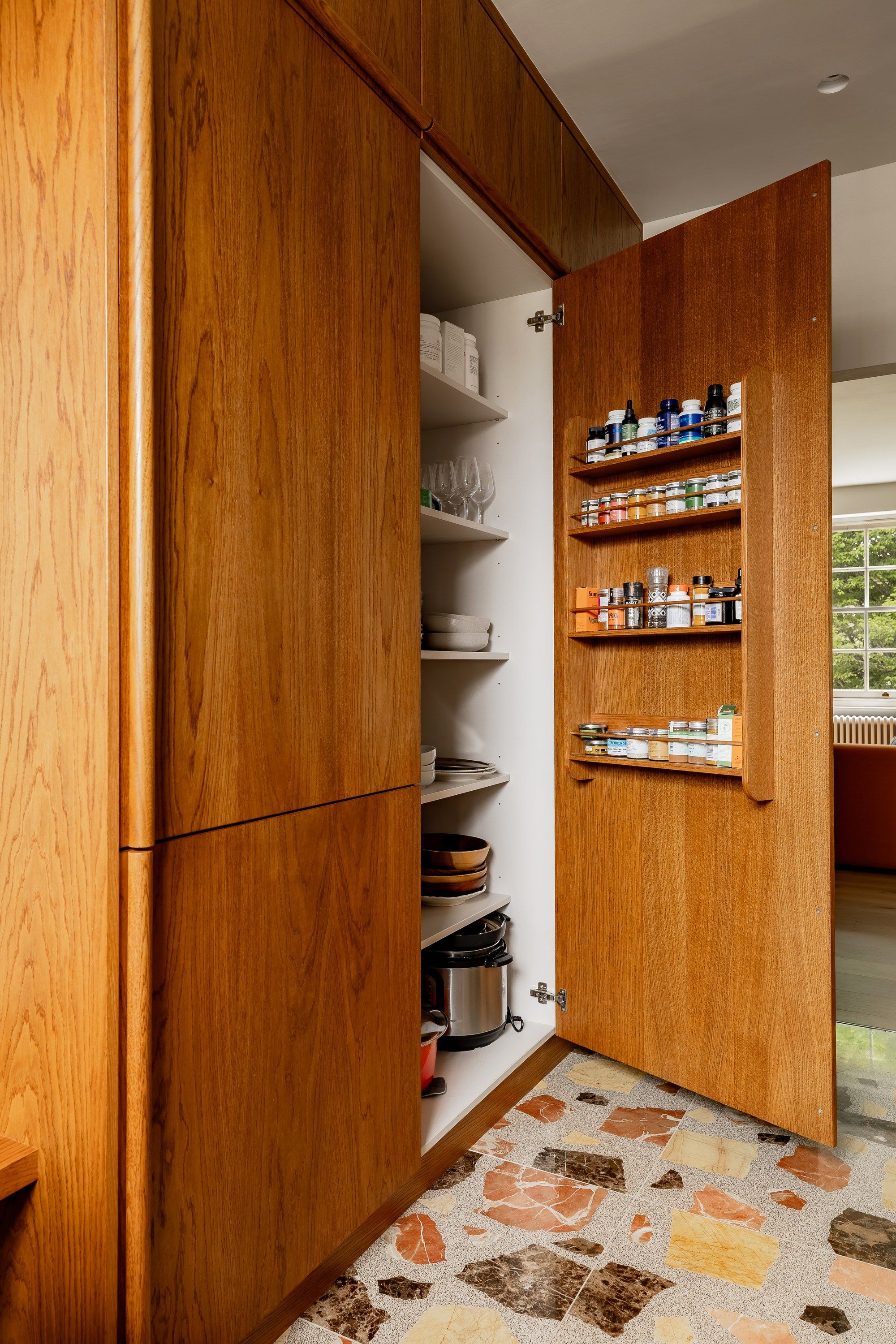A tall wooden larder standing open, its door racks lined with jars and spices.
