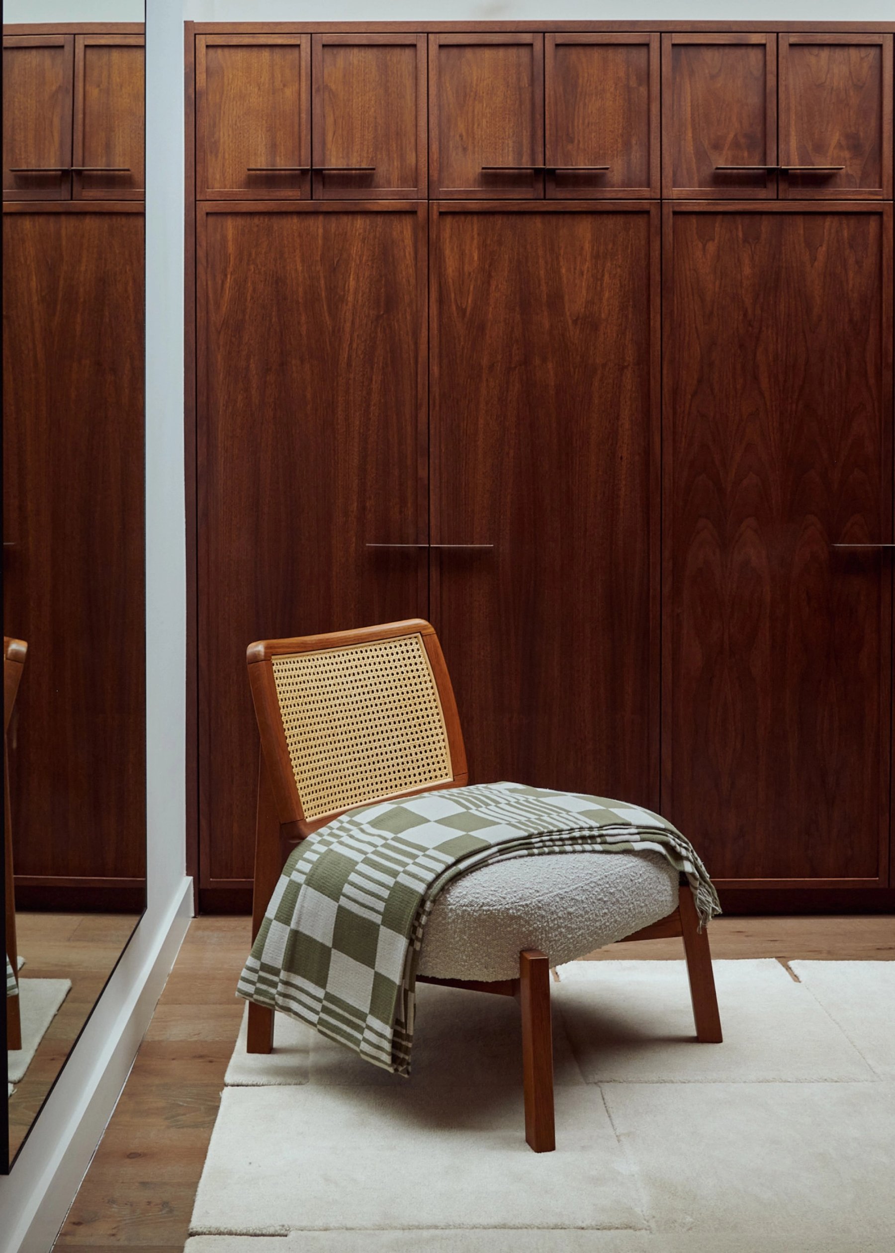 Dressing room detail: walnut wardrobes with slim recessed handles and a caned lounge chair with a green checked throw on a pale rug.