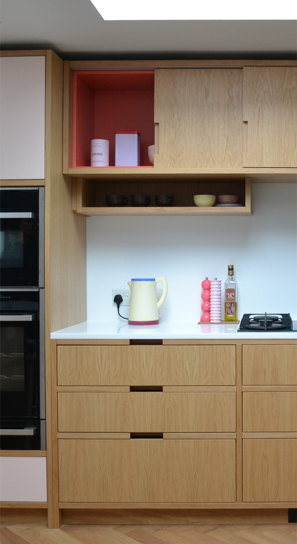 Oak wall cabinets with a coral painted interior above a white worktop and gas hob, over deep oak drawers