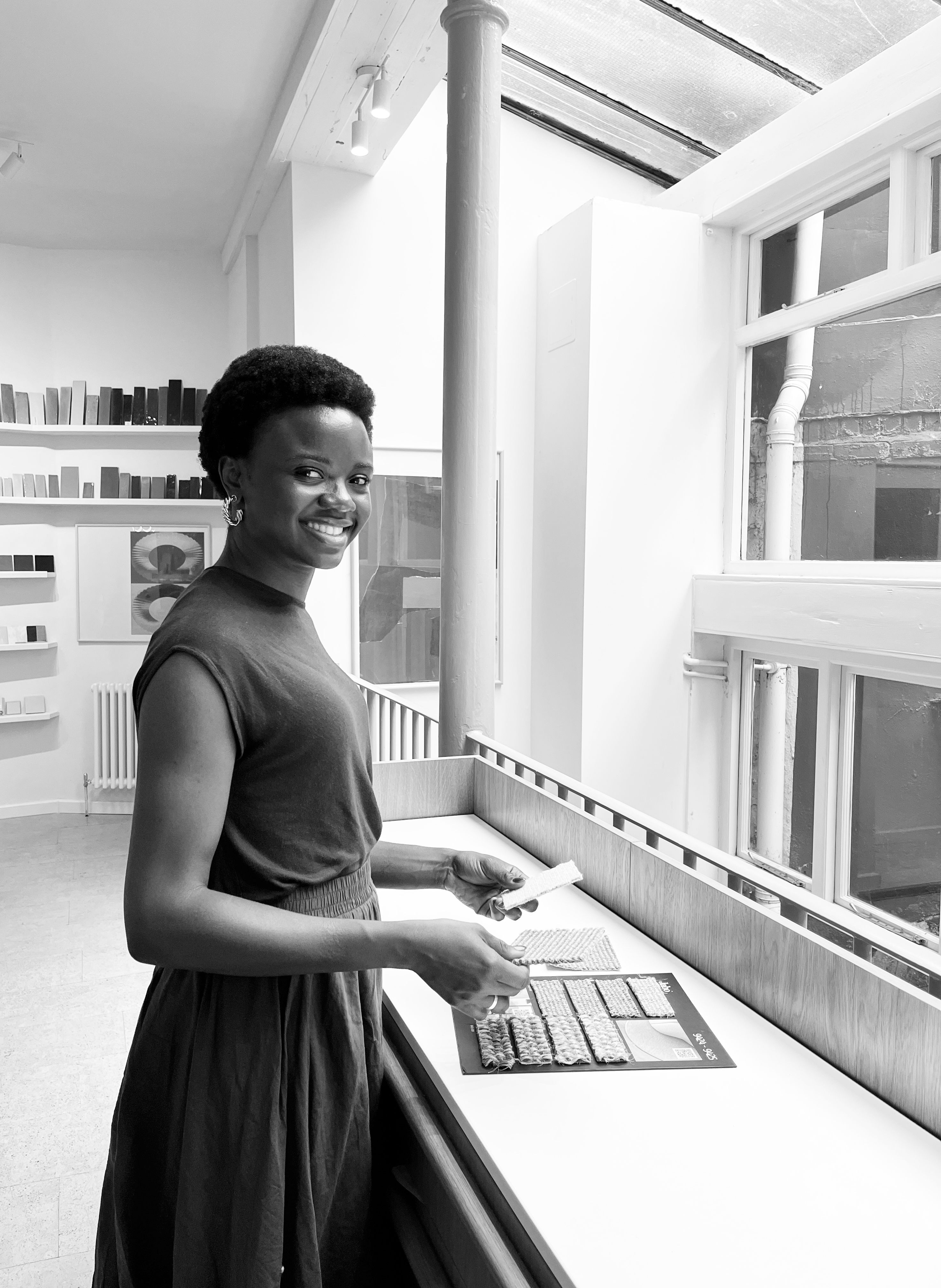 Funke Oduwole, smiling, laying out fabric samples on a long counter beneath a skylight in the studio.