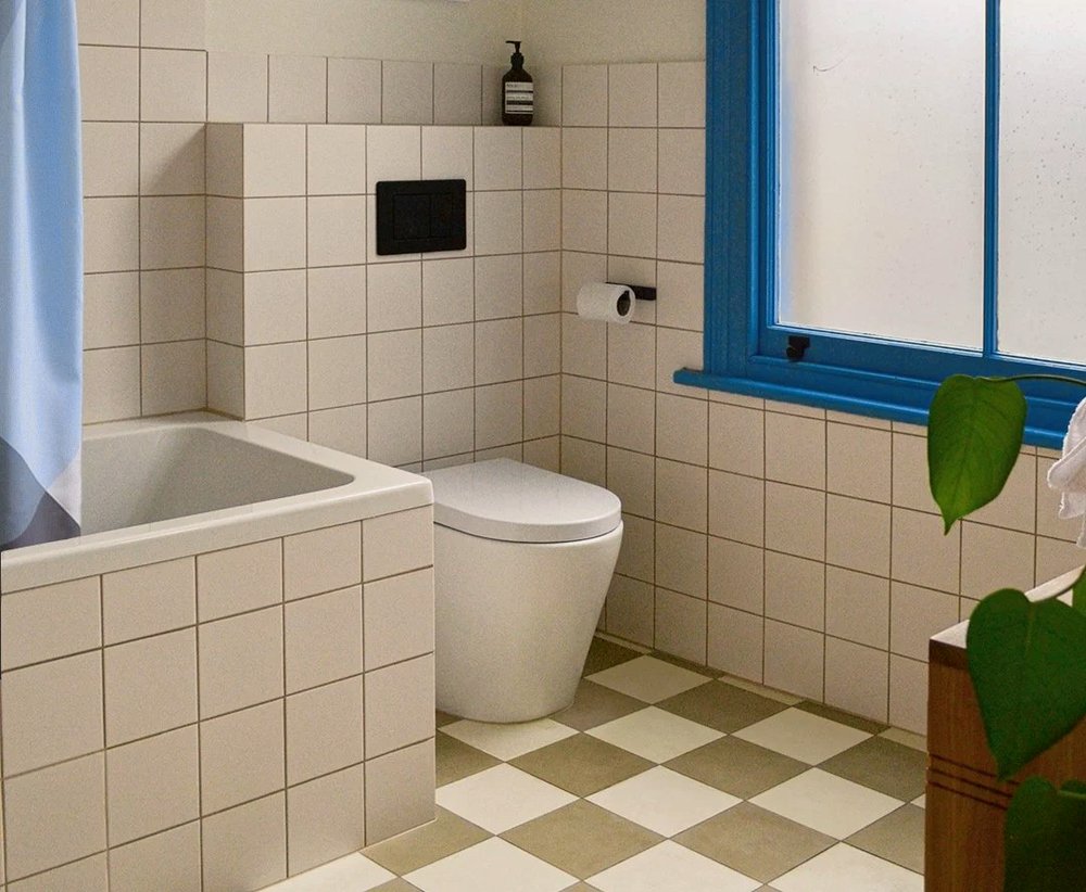 Bathroom with square white wall tiles, a cobalt blue painted window frame, tiled bath surround and olive and cream chequerboard floor tiles