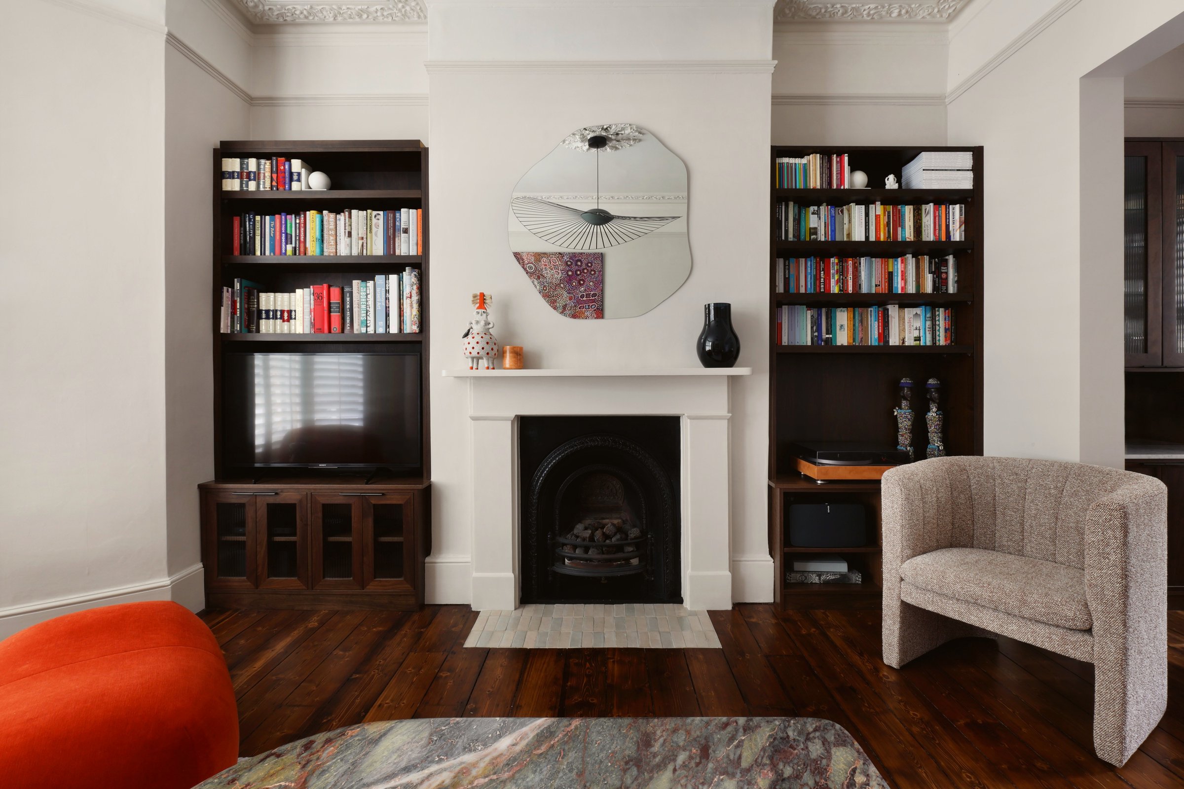 White fireplace with a black arched insert and logs in the grate, an organic-shaped mirror above, and dark stained bookcases built into both alcoves.