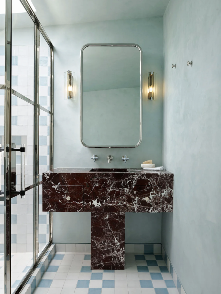 Pale blue bathroom with a burgundy marble pedestal vanity, a chrome-framed mirror and blue and white checked floor tiles