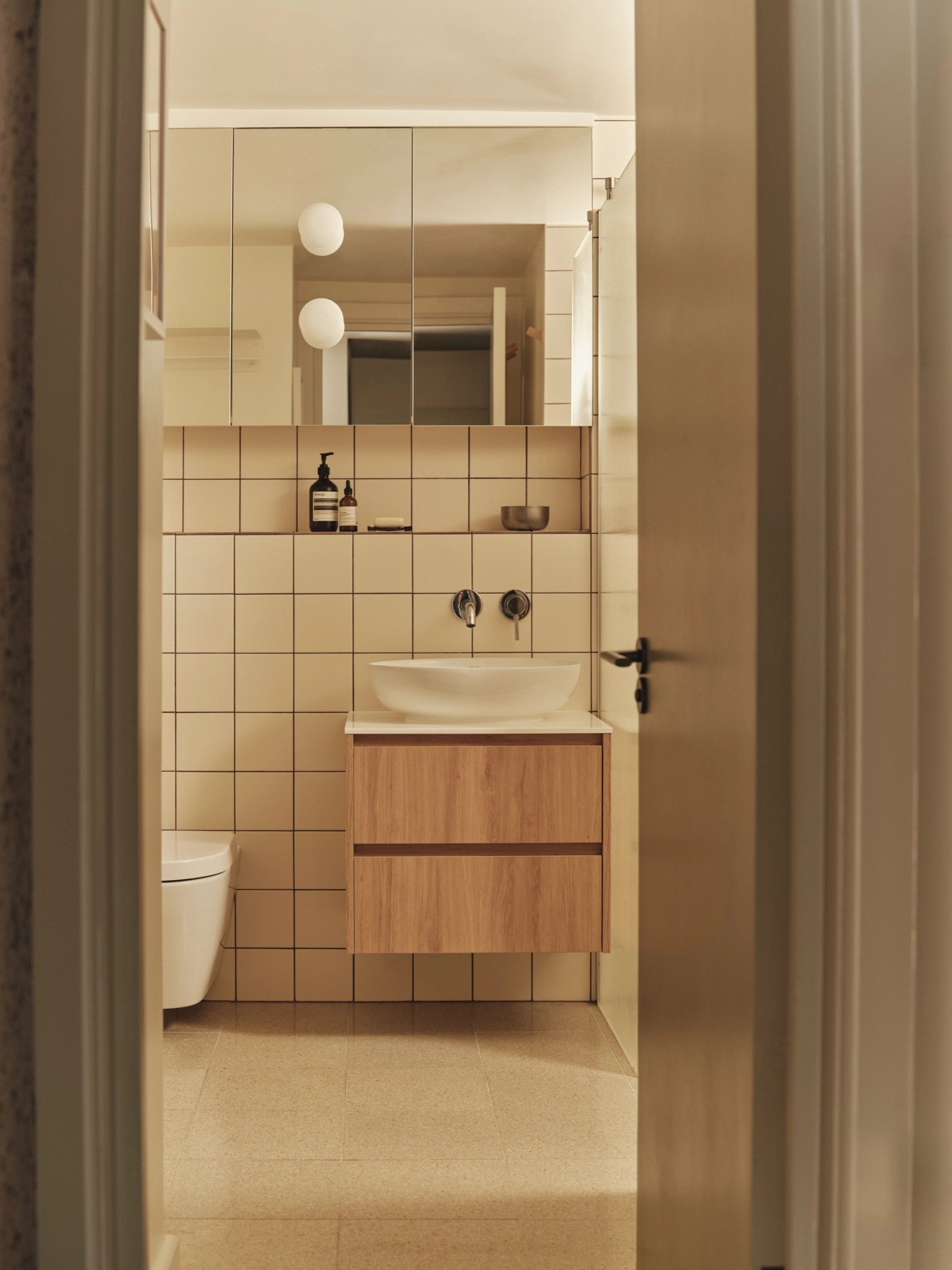 Shower room through the doorway: a round basin on an oak wall-hung vanity, chrome wall mixer and a mirrored cabinet with globe lights above.