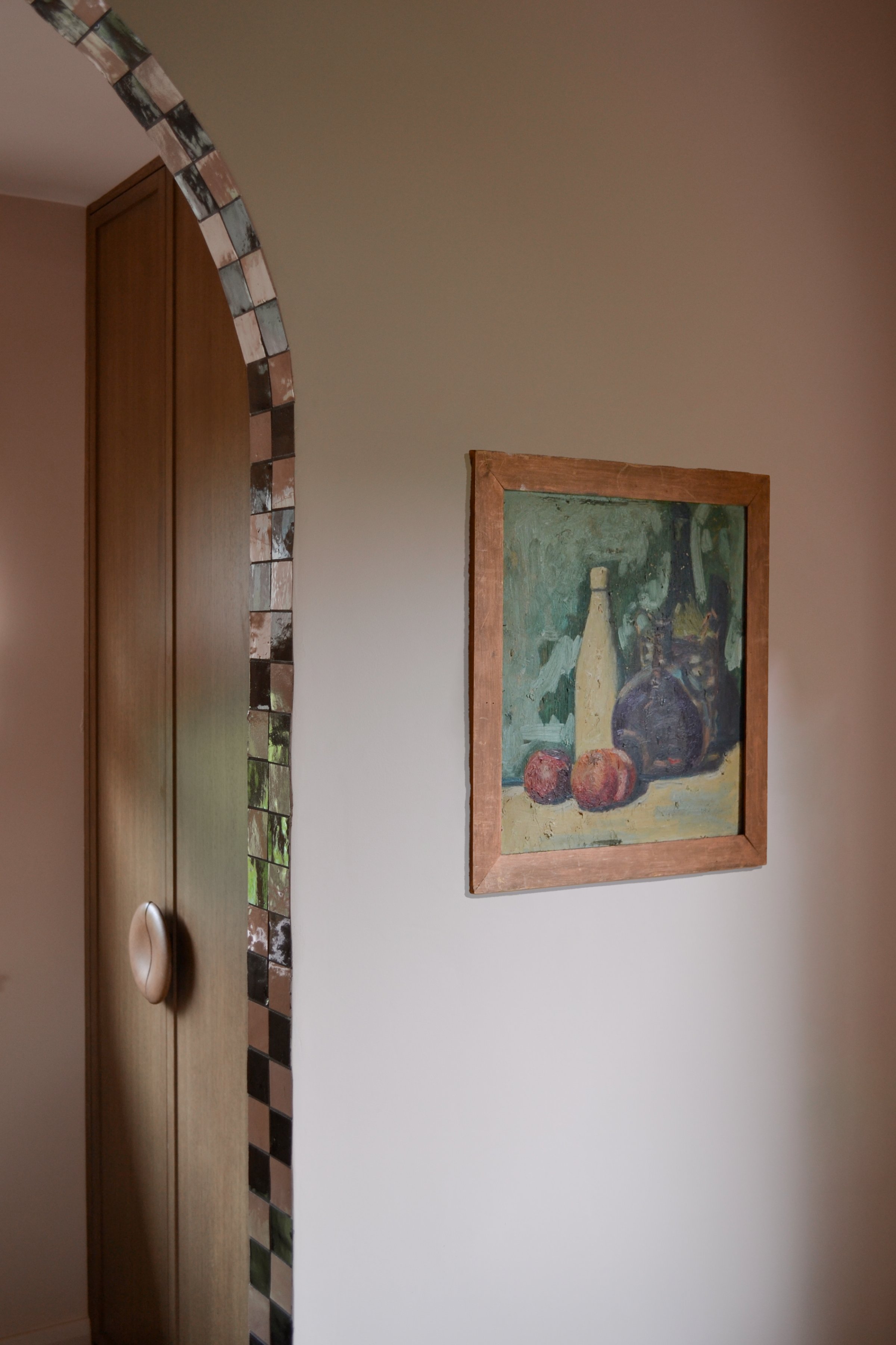Oak wardrobe with a carved round handle beside an arched opening trimmed in black and white chequerboard mosaic