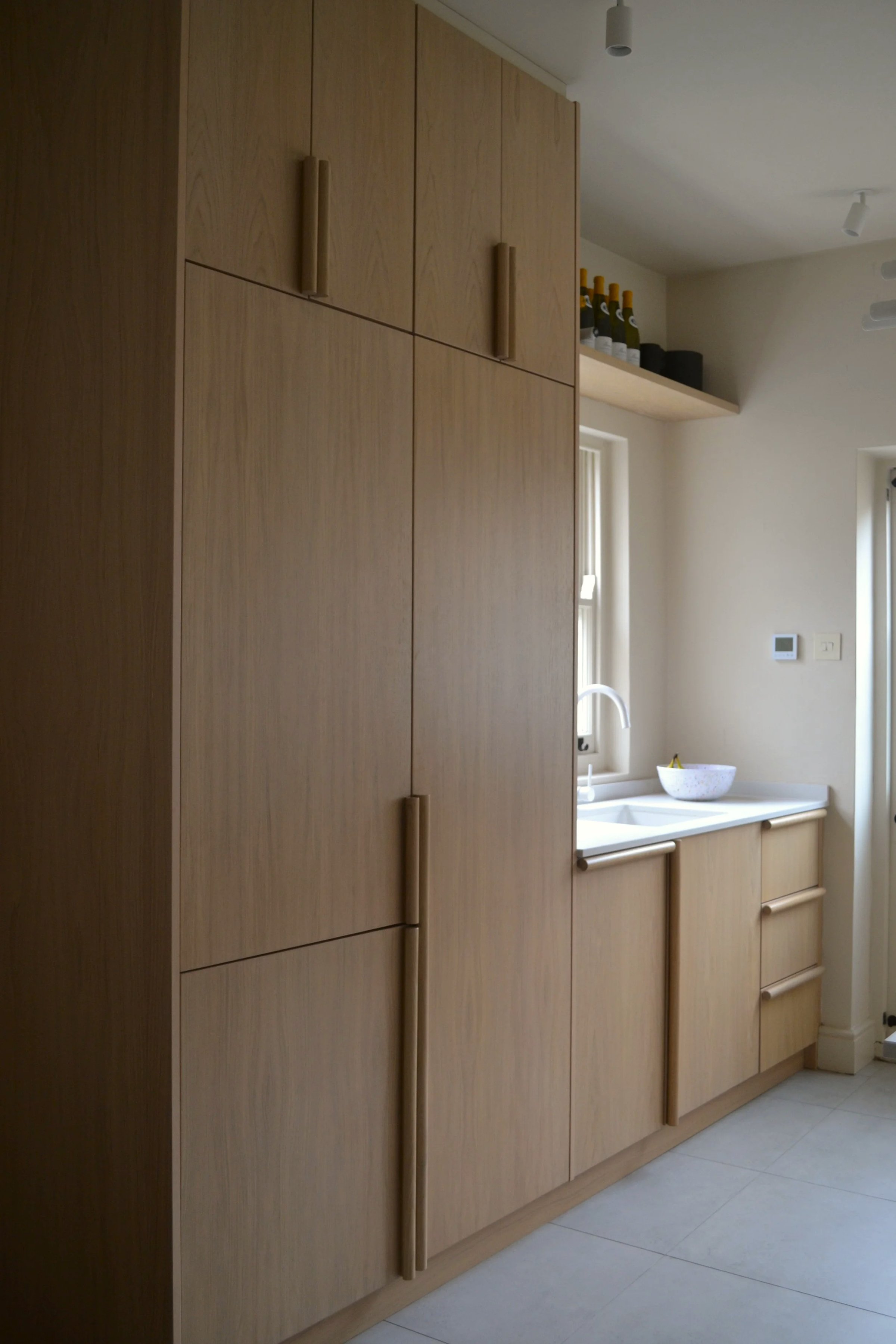 Full-height pale oak cabinetry running to the ceiling beside a sink set under a window