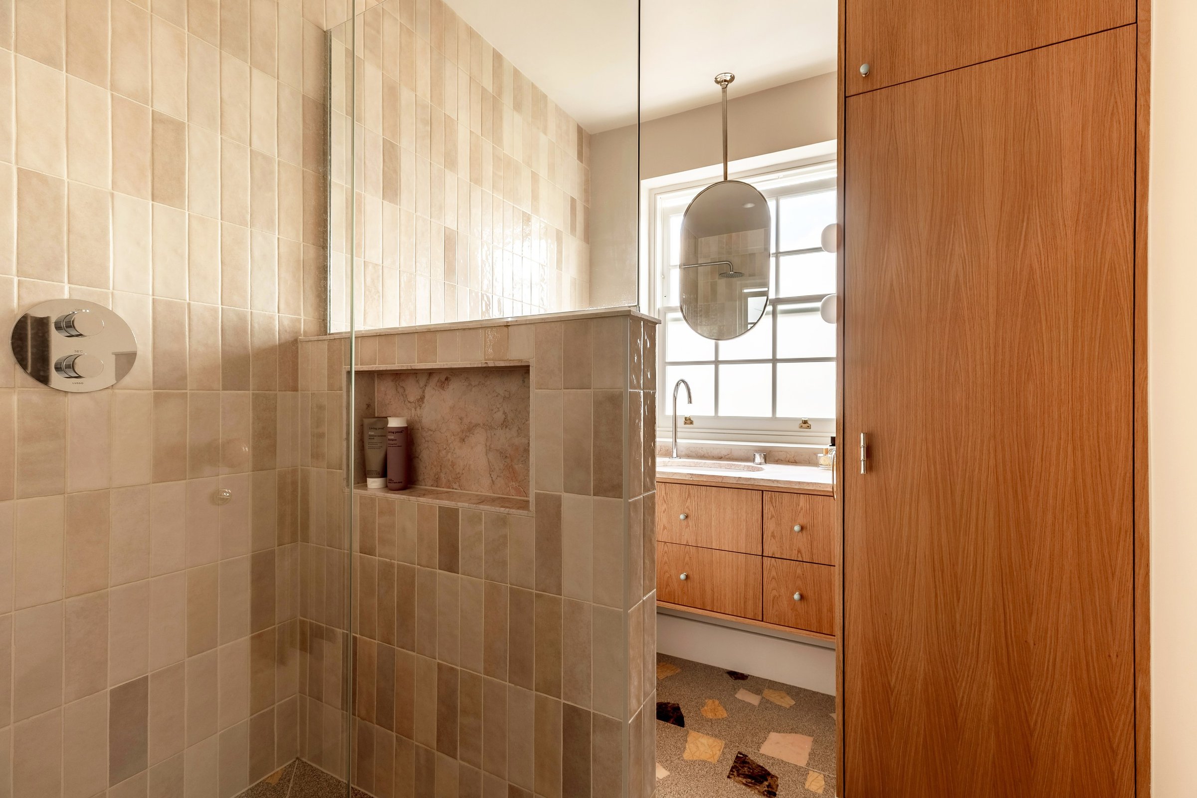 Bathroom with a walk-in shower behind a tiled half wall with a niche, beside a tall wooden cabinet.