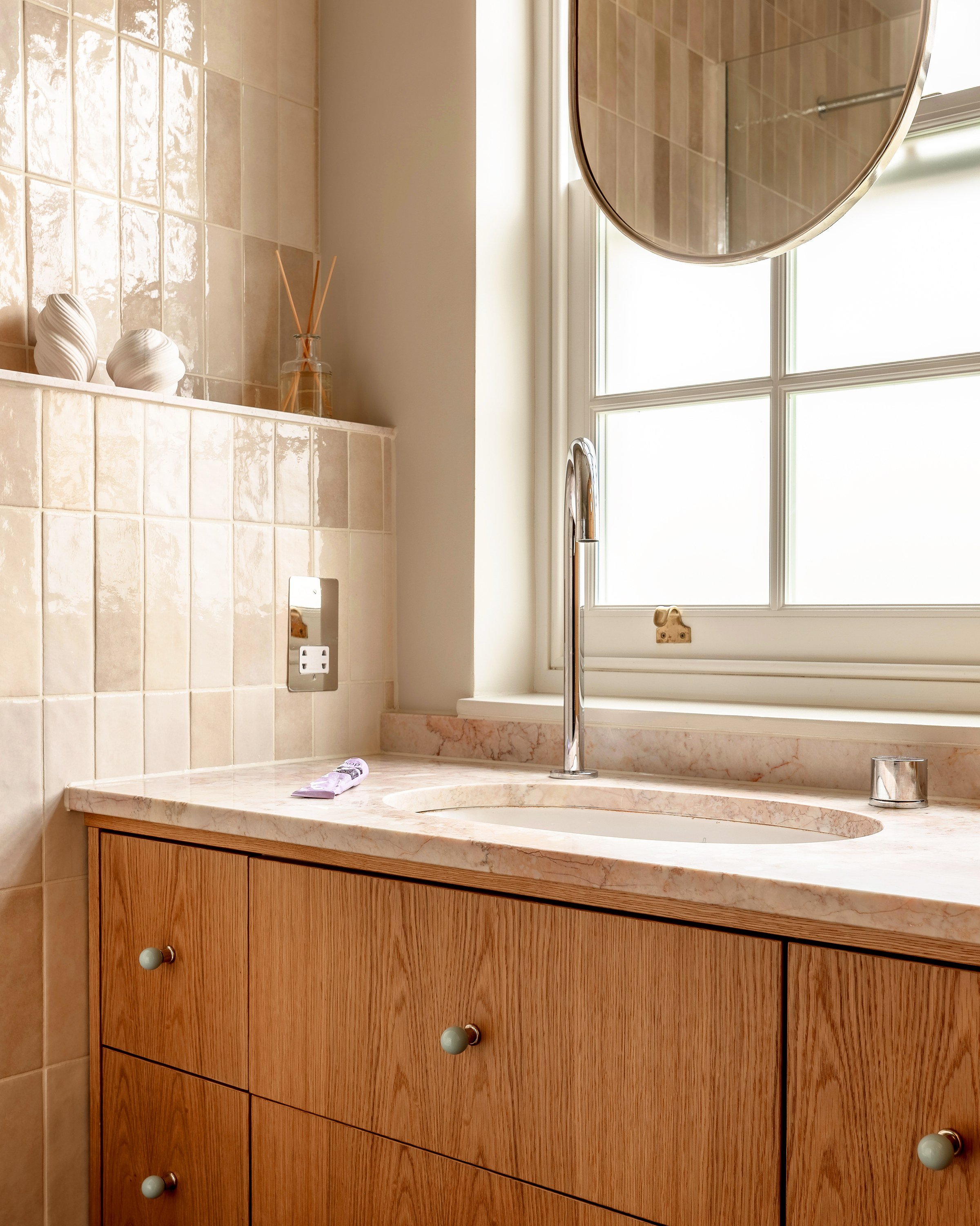 Basin set into a pale stone top beneath a sash window, with handmade tiles and small objects on a ledge.