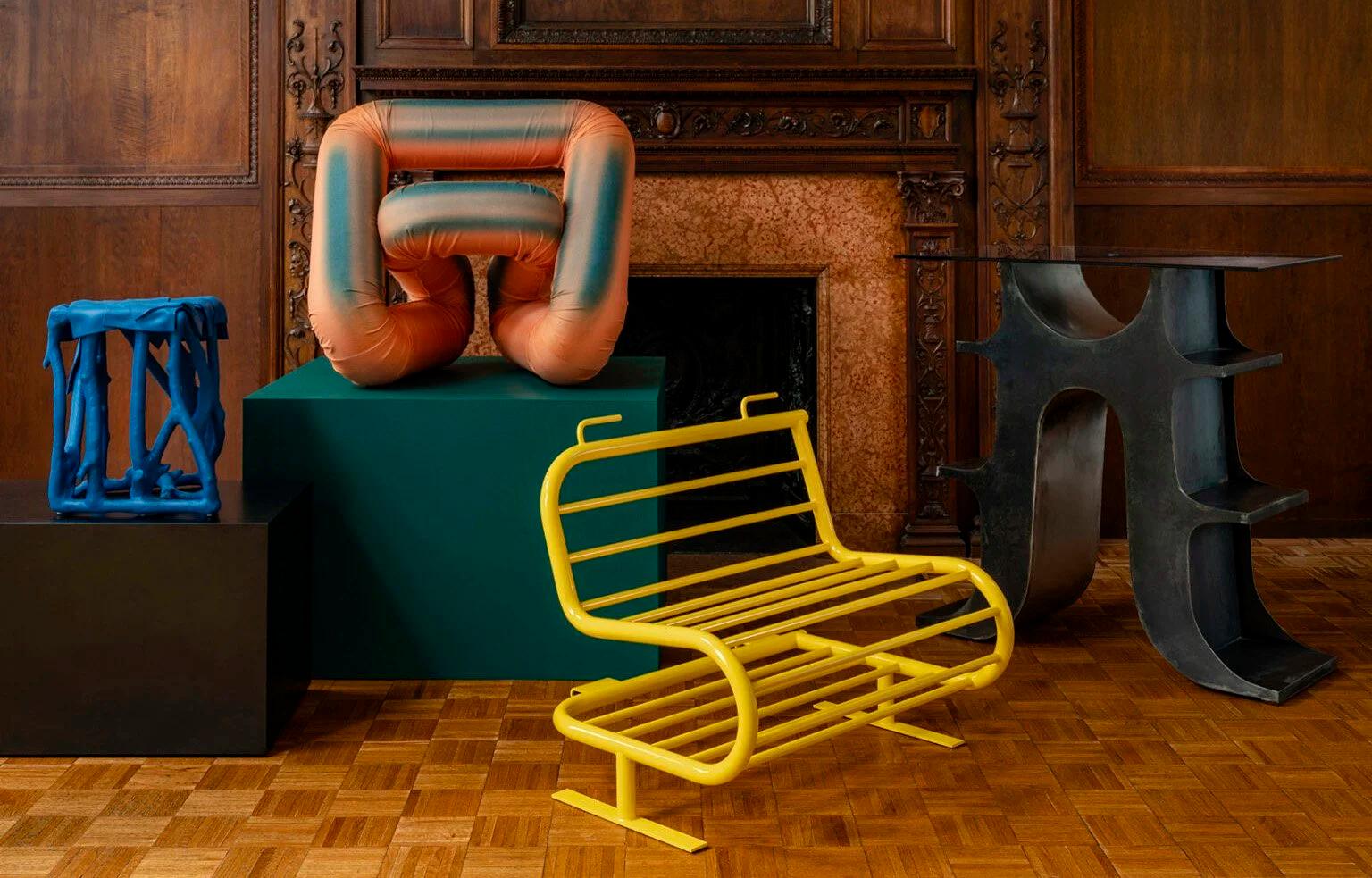 Panelled room with a carved stone fireplace, a yellow tubular steel bench, a padded terracotta form on a green plinth and a blue lattice stool