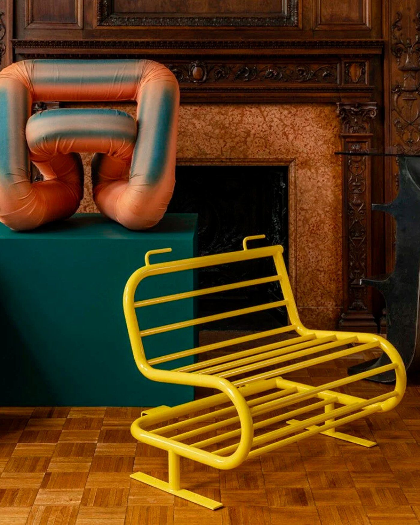 Panelled room with a carved stone fireplace, a yellow tubular steel bench, a padded terracotta form on a green plinth and a blue lattice stool