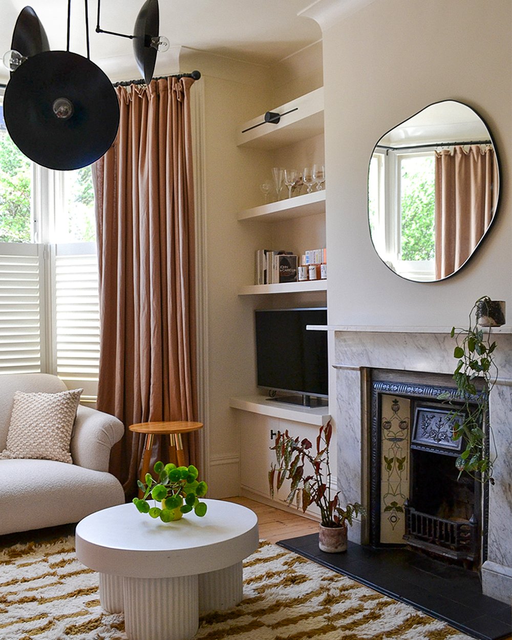 Sitting room with a marble fireplace and decorative tiled insert, alcove shelving, a round mirror and a fluted white coffee table