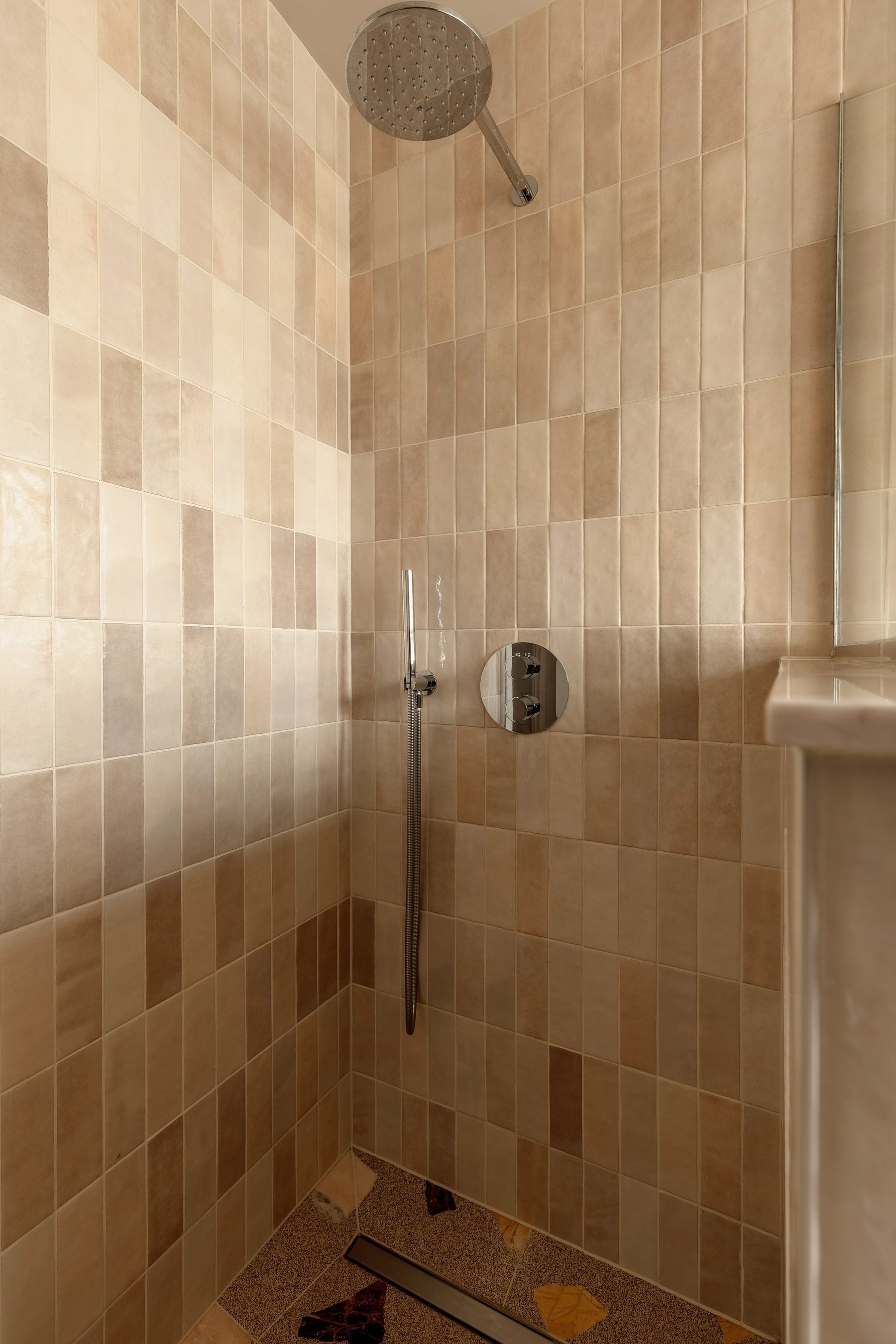 Walk-in shower lined in handmade tiles of soft pink and sand, with a rainfall head and a linear drain.