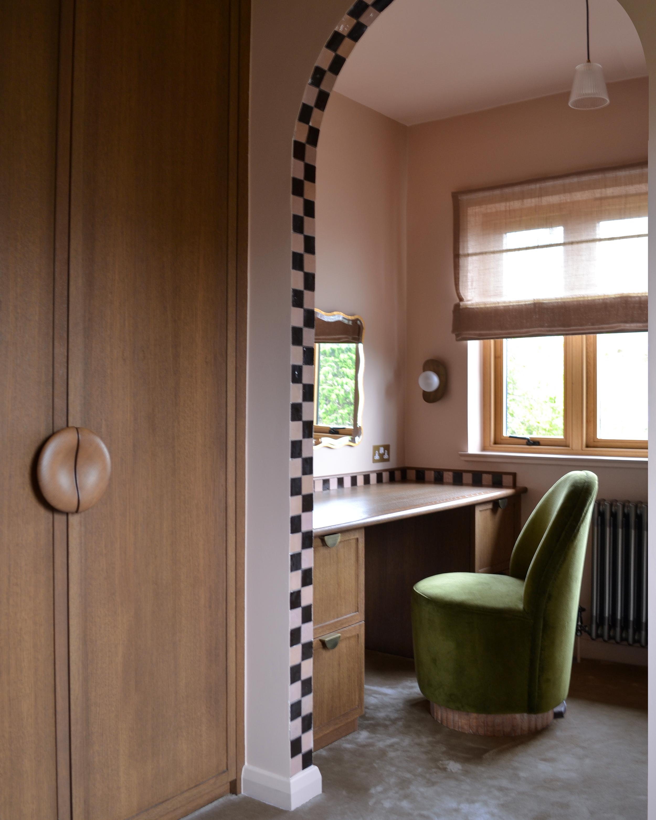 Dressing room seen through the chequerboard arch, with fitted oak wardrobes, a built-in desk and a green velvet chair at the window