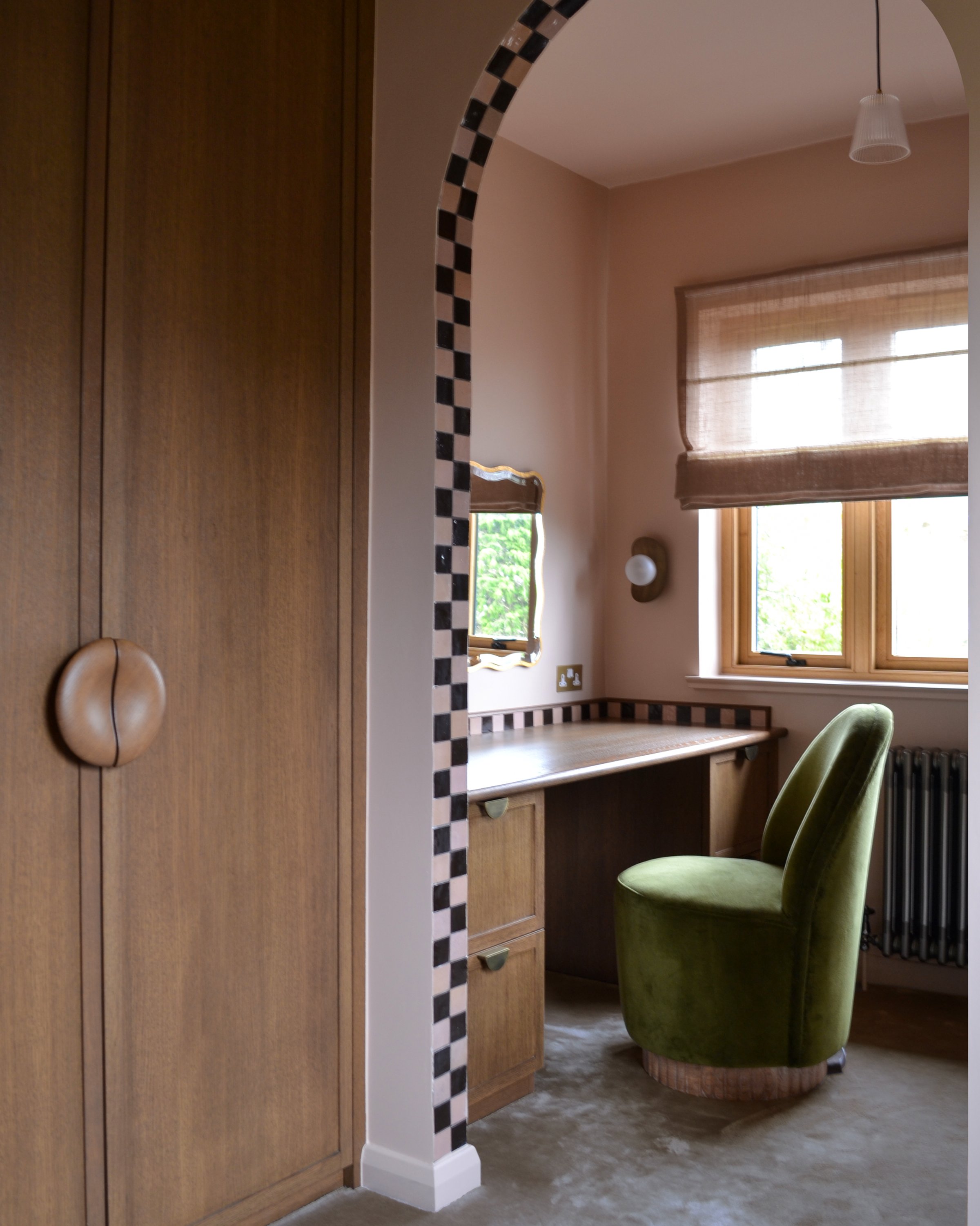 Dressing room seen through the chequerboard arch, with fitted oak wardrobes, a built-in desk and a green velvet chair at the window
