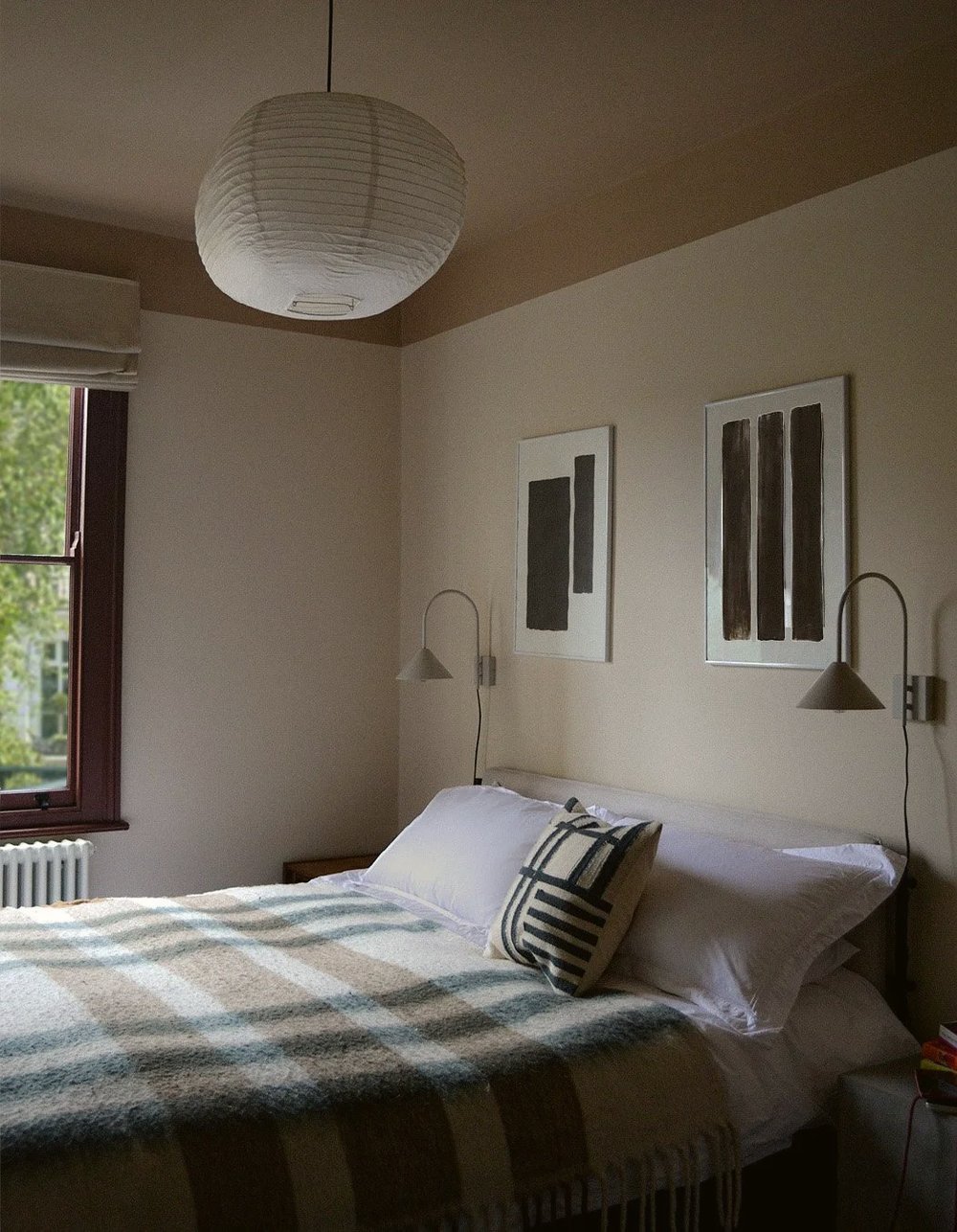 Bedroom with a paper globe pendant, adjustable wall reading lights either side of the bed and a checked wool blanket