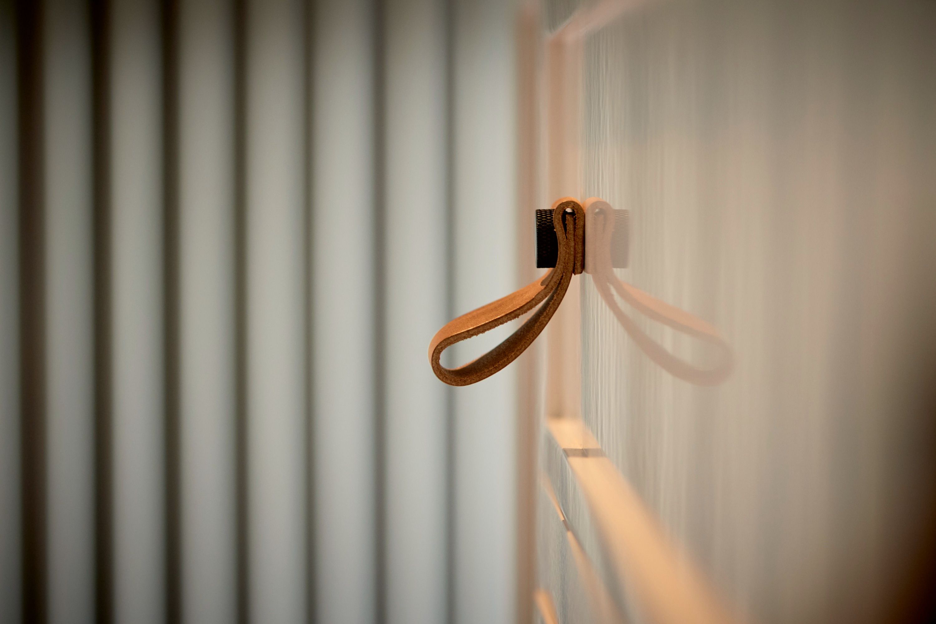 Close detail of a leather pull loop fixed to a pale cabinet door, with fluted glass out of focus behind it.