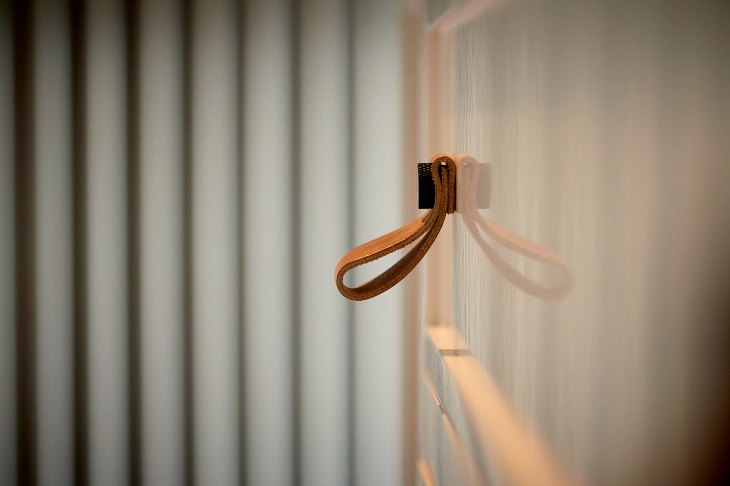 Close detail of a leather pull loop fixed to a pale cabinet door, with fluted glass out of focus behind it.