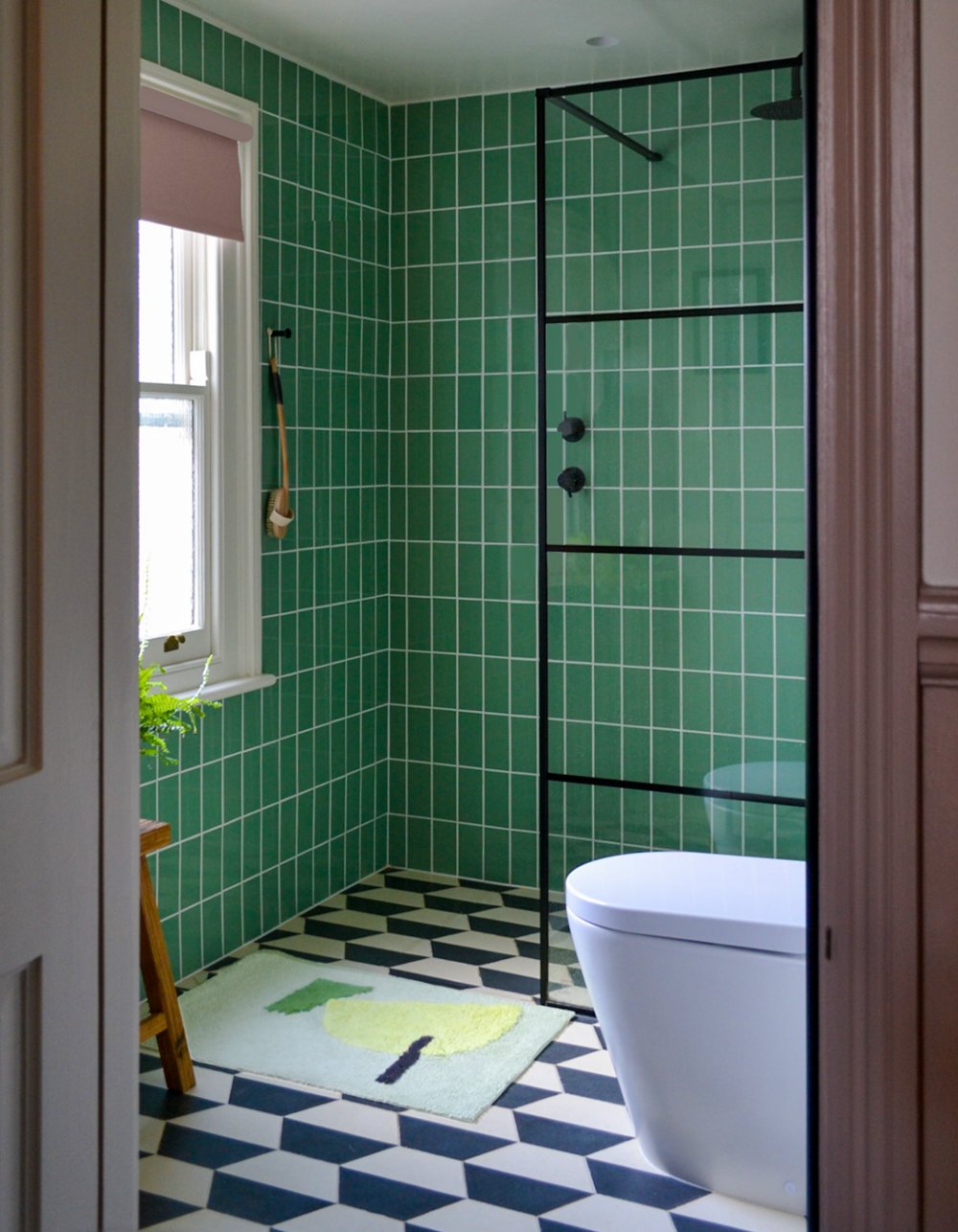 Family bathroom tiled floor to ceiling in green square tiles, with a black-framed shower screen and a black and white chequerboard floor