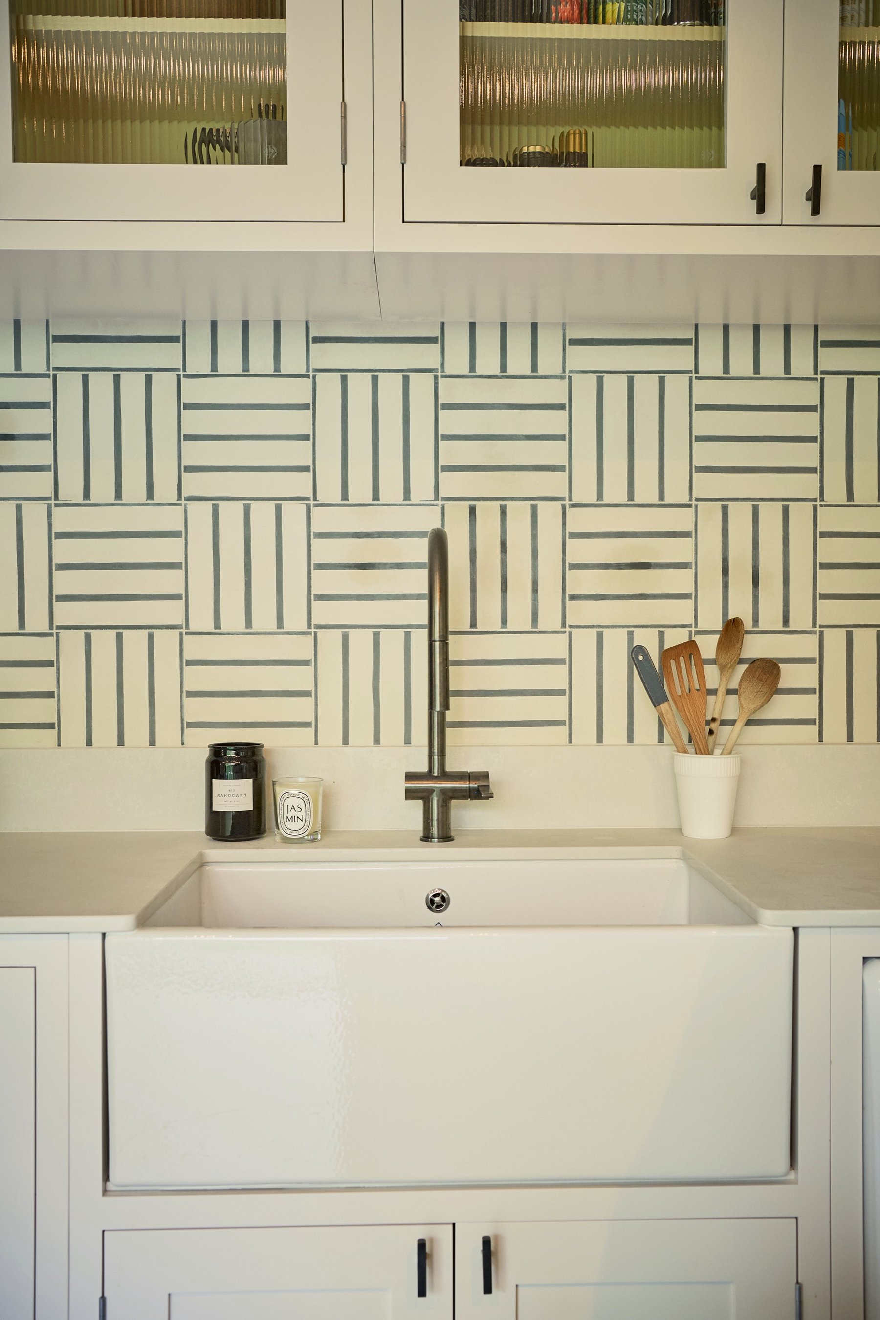 Butler sink and gunmetal tap under a monochrome basketweave splashback, with reeded glass wall cupboards above.