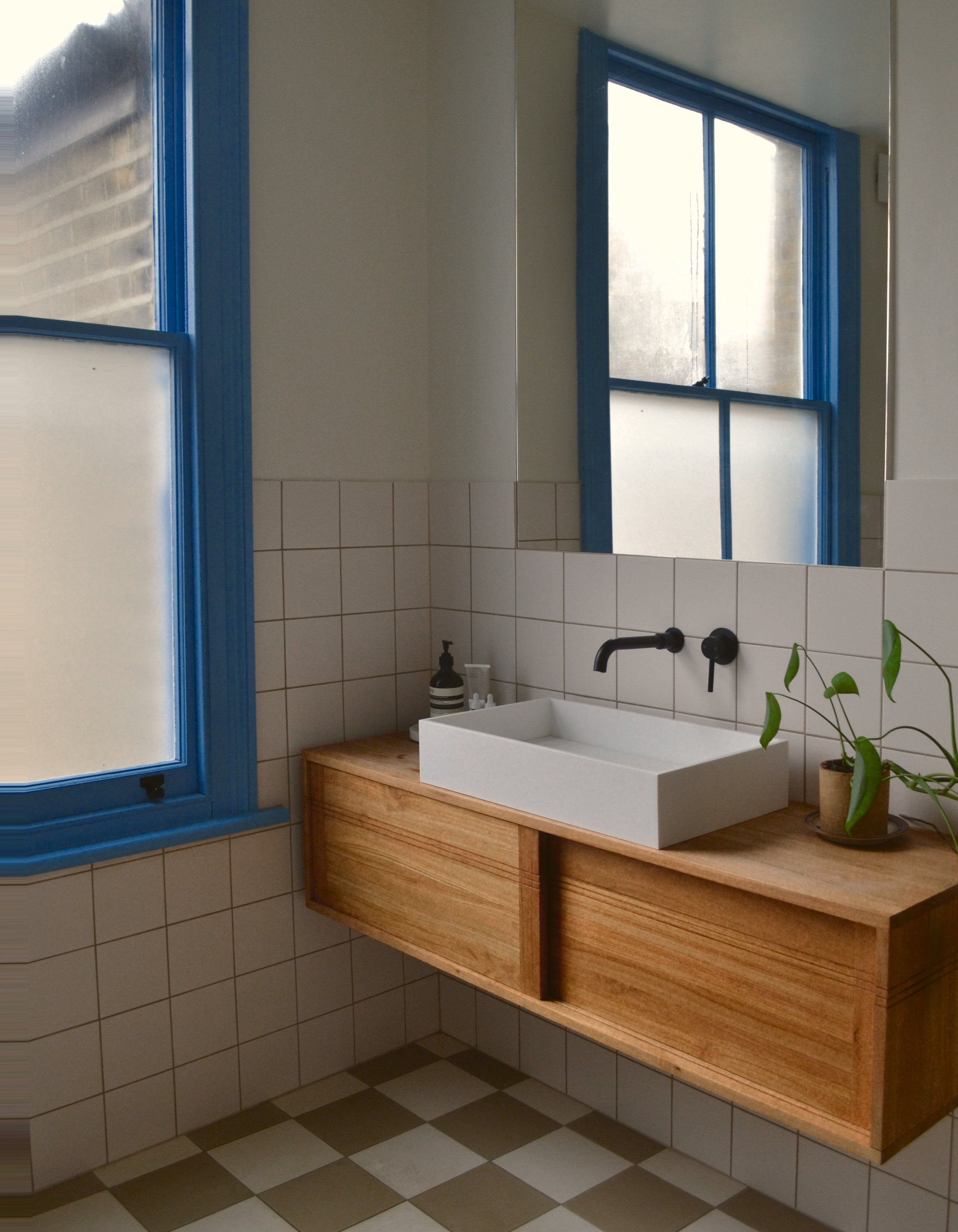 Bathroom with an oak floating vanity, white countertop basin and black wall-mounted tap, framed by blue painted sash windows