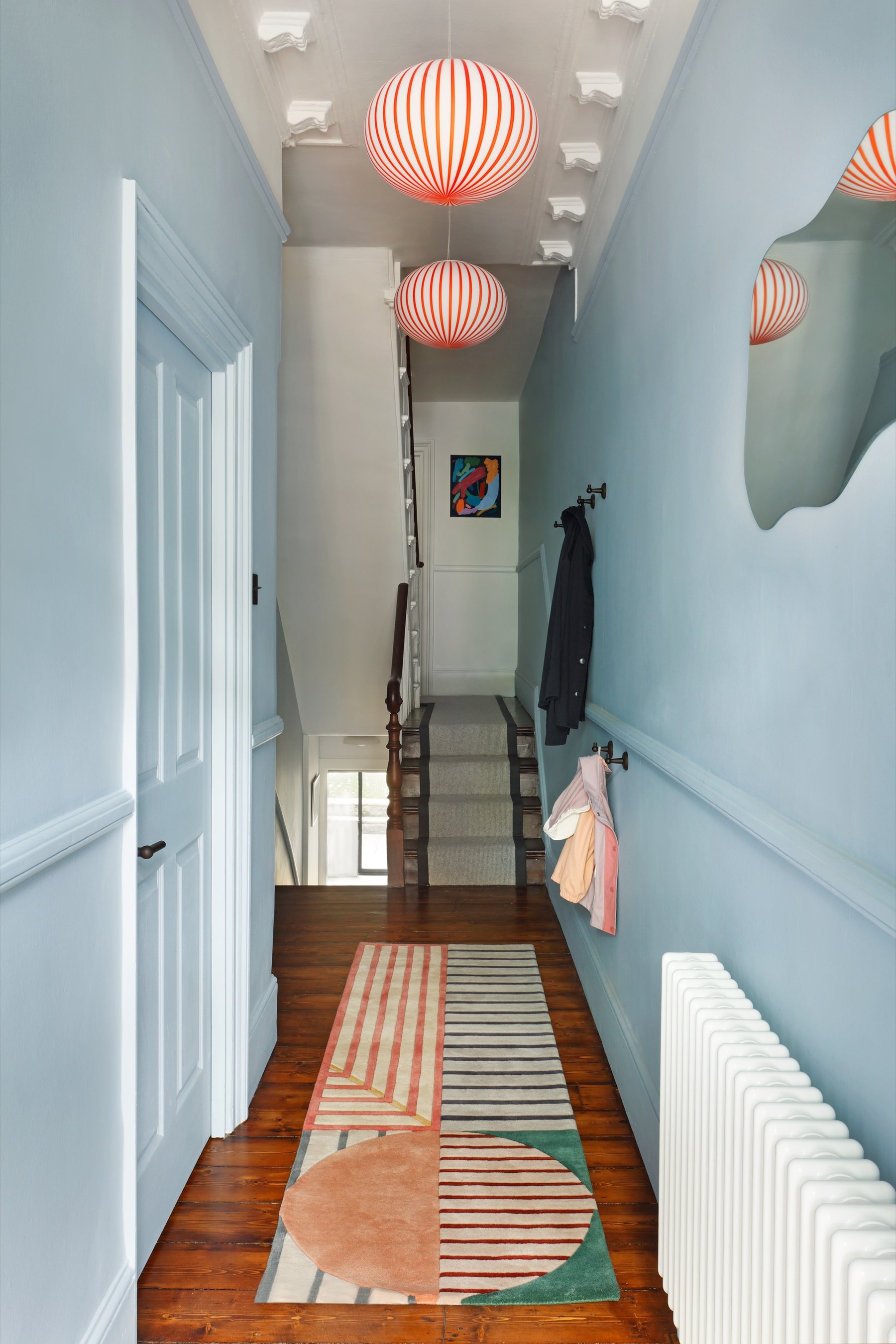 Hallway painted pale blue to the picture rail, with two red and white striped globe pendants and a terracotta and green runner along dark boards.