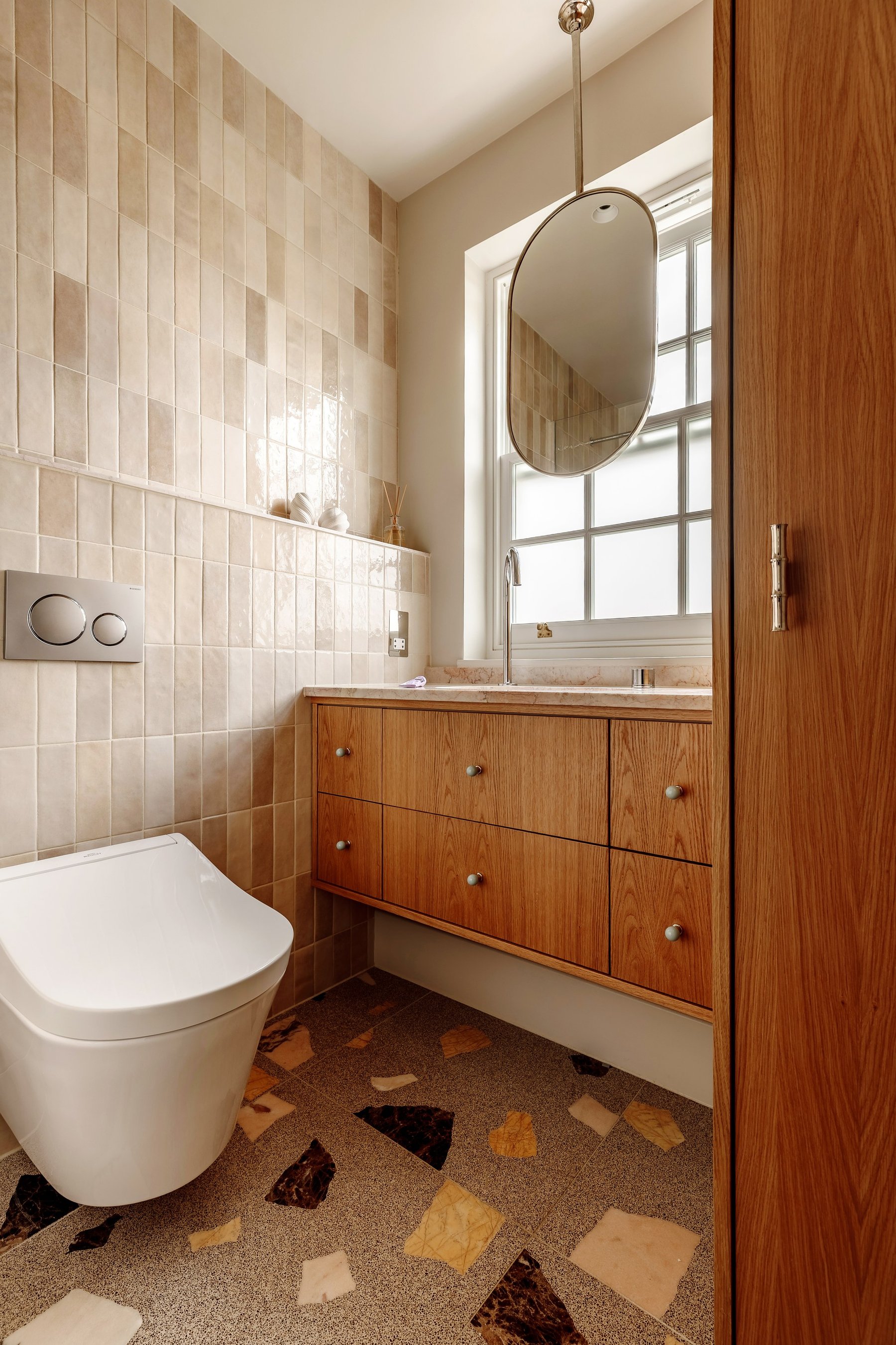 Bathroom with a wooden vanity of drawers under a pale stone top, a wall-hung toilet, handmade tiles and a terrazzo floor.