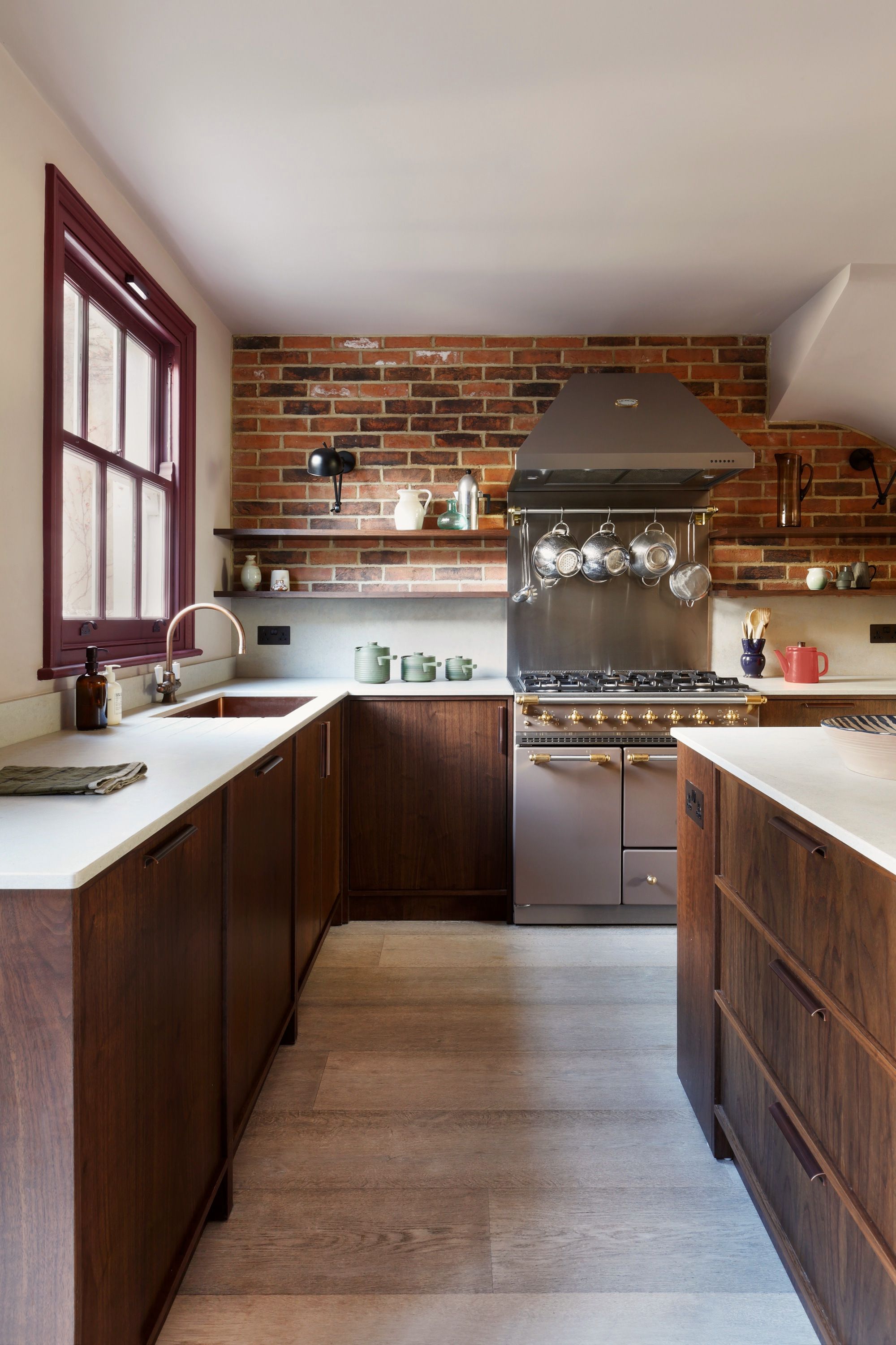 Kitchen with dark stained timber cabinets both sides, a stainless range against an exposed brick chimney breast and copper pans on a rail.