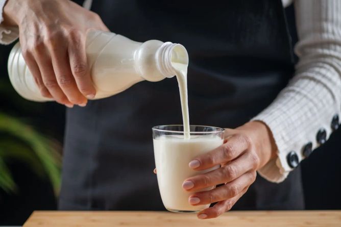 Nalévání hustého kefíru z lahve do sklenice na kuchyňském stole Nalévání hustého kefíru z lahve do sklenice na kuchyňském stole