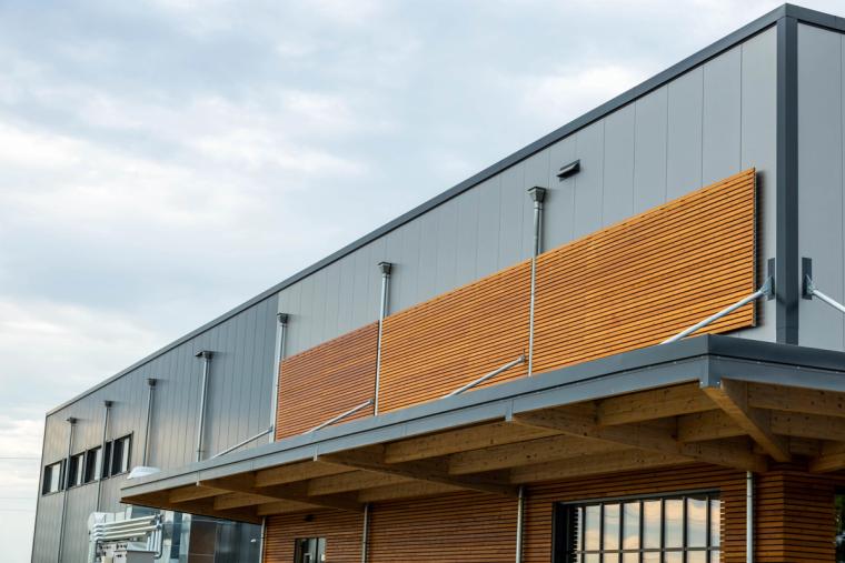 Obergeschoss-Fassade mit horizontalem Holzlamellen-Band in der grauen Wand, darunter ein auskragendes Vordach aus Brettschichtholz
