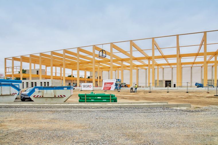 Rohbau der Logistikhalle mit dem Tragwerk aus Holzstützen und Trägern, davor das SEGRO-Bauschild und ein Teleskoplader