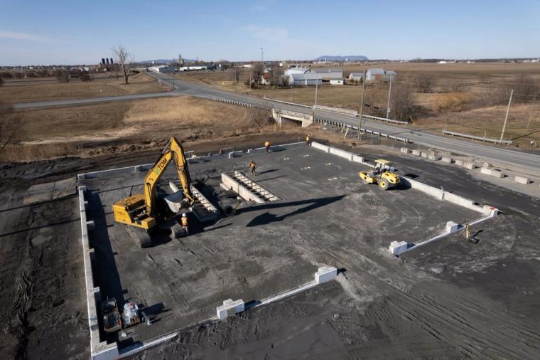 Vue aérienne du chantier en plaine avec les fondations creusées et une pelle mécanique