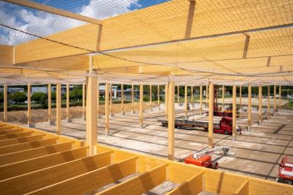 Blick von oben über das Holzdach-Tragwerk der Logistikhalle, Träger im Raster, Hebebühnen auf der Baustelle darunter