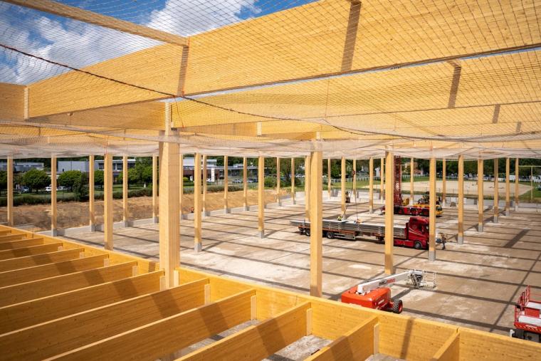 Blick von oben über das Holzdach-Tragwerk der Logistikhalle, Träger im Raster, Hebebühnen auf der Baustelle darunter
