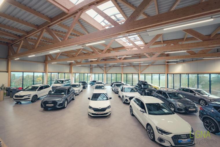 Heller Showroom mit zahlreichen Neuwagen und umlaufender Fensterfront unter sichtbaren Holzbindern