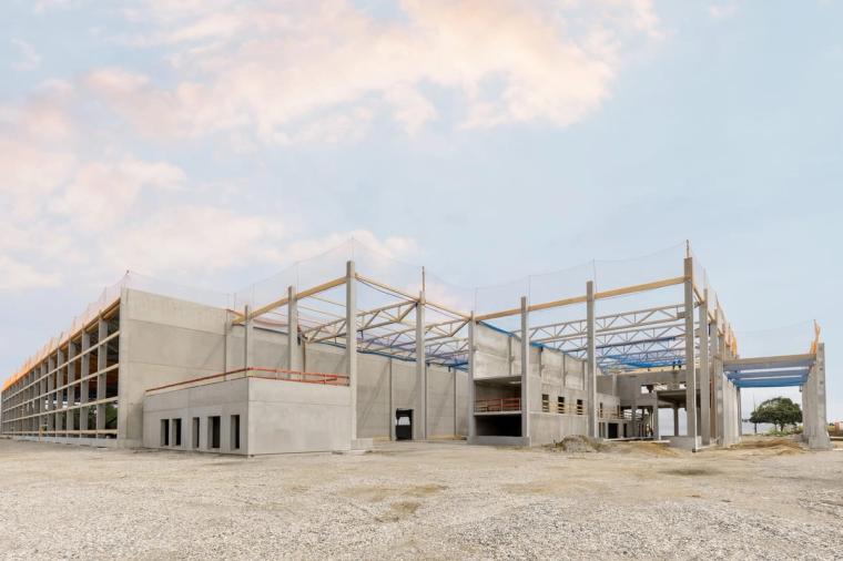 Shell of the hall at dusk, precast concrete columns with the first timber trusses installed and safety nets in place