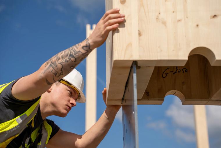 Monteur richtet den Kopf einer Holz-Rohrstütze aus, Kastenquerschnitt sichtbar