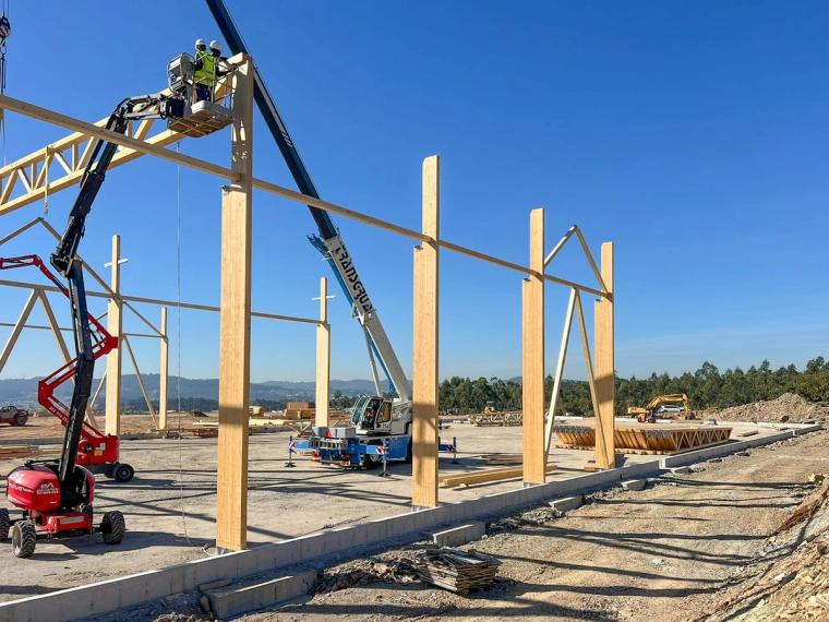 Monteure auf einem Hubsteiger befestigen Stützen und Aussteifungen des Holztragwerks