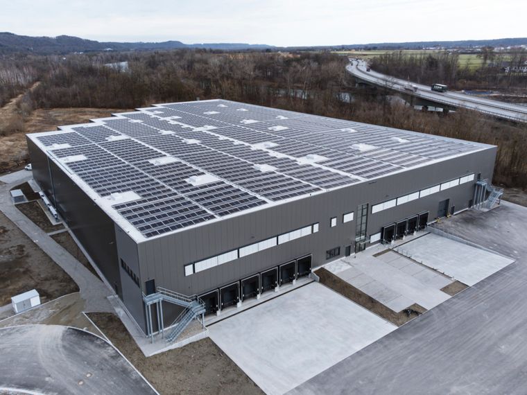 Luftaufnahme der Logistikhalle mit vollständig belegtem Photovoltaikdach, Laderampen an der Längsseite und weitläufigem Außengelände.