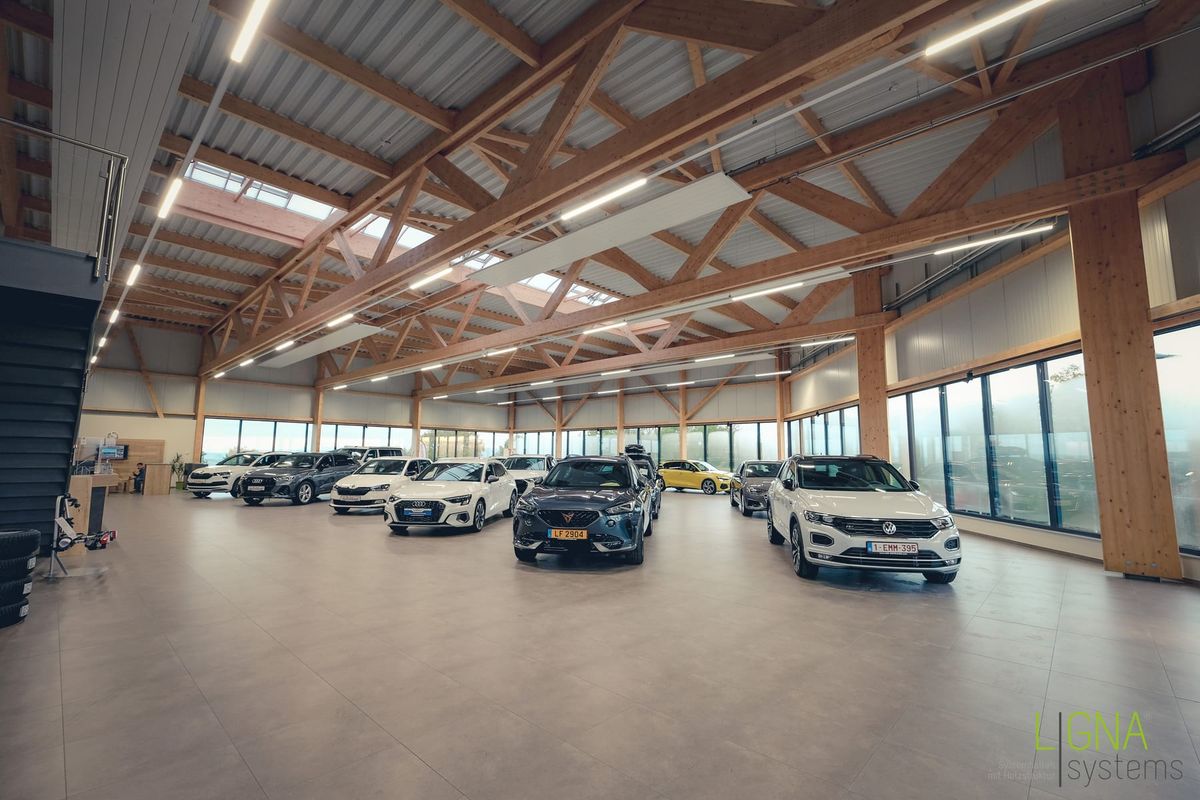 Weiter Showroom des Autohauses mit Pkw-Reihen unter einem sichtbaren Holzdach aus Fachwerkbindern