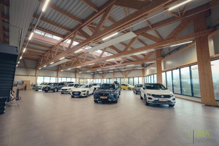 Weiter Showroom des Autohauses mit Pkw-Reihen unter einem sichtbaren Holzdach aus Fachwerkbindern