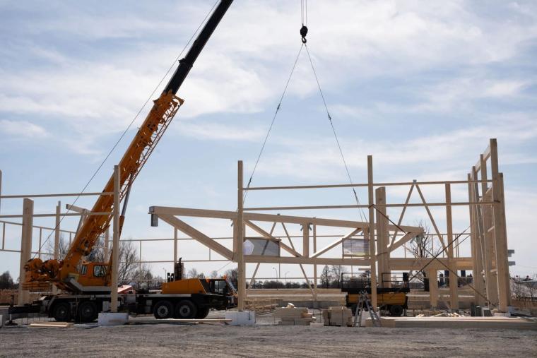 Une grue mobile soulève une ferme en lamellé-collé au-dessus du chantier dans le vaste paysage