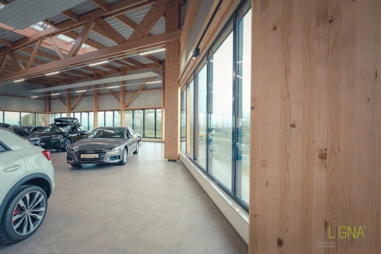 Showroom-Ecke mit Sichtholzstütze, raumhoher Glasfassade und ausgestellten Fahrzeugen