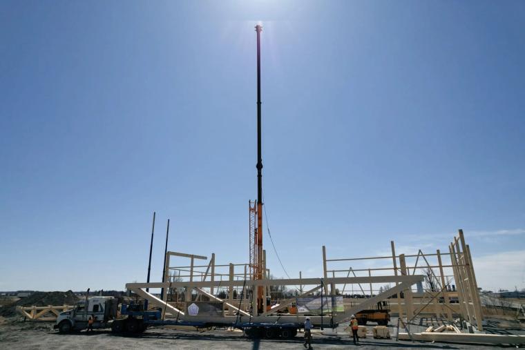 Vue aérienne du montage de l’ossature en cours, avec grue mobile et squelette en bois partiellement dressé