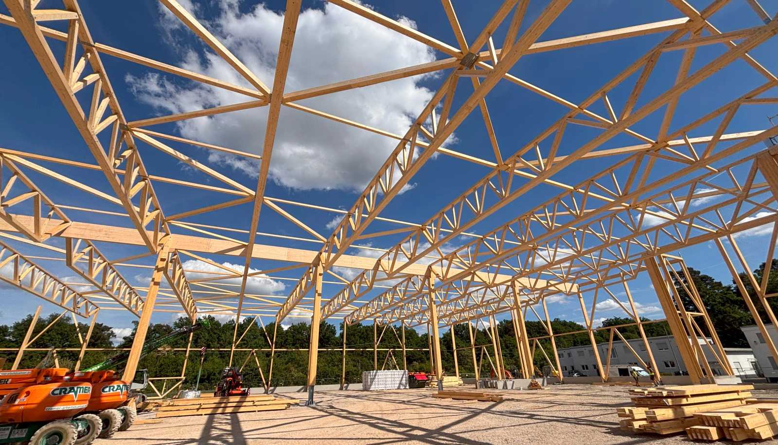 Weitgespannte Holz-Fachwerkbinder einer Halle während der Montage unter blauem Himmel
